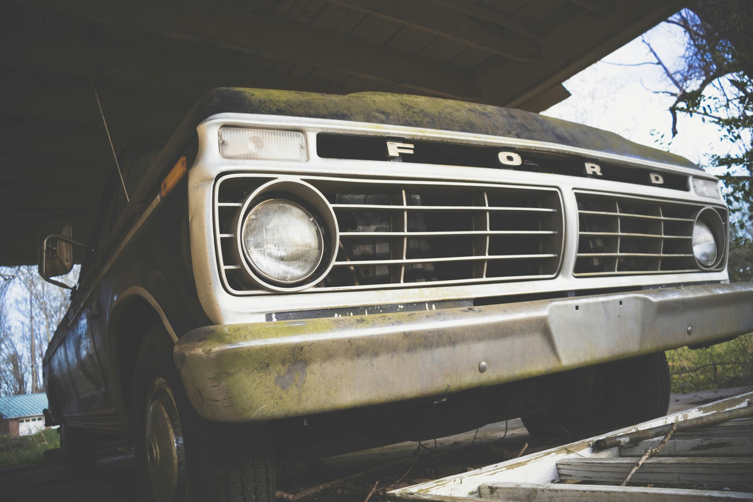 Front of an 1986 Ford truck under a canopy, headlights off.
